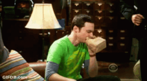 A Man In A Green Shirt Is Sitting On A Couch And Eating A Bag Of Food . GIF