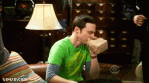 A Man In A Green Shirt Is Sitting On A Couch Eating From A Bag . GIF