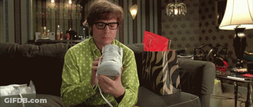 A Man In A Green Shirt Is Sitting On A Couch Holding A Shoe GIF