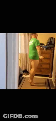 A Man In A Green Shirt Is Standing In A Hallway . GIF