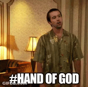 A Man In A Green Shirt Is Standing In A Living Room With The Words Hand Of God Written On The Screen . GIF