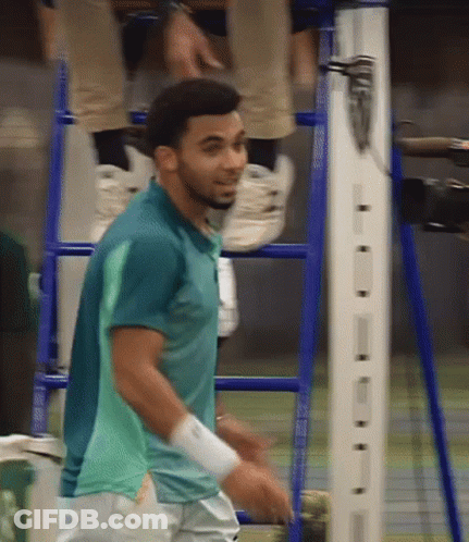 A Man In A Green Shirt Is Standing In Front Of A Ladder GIF