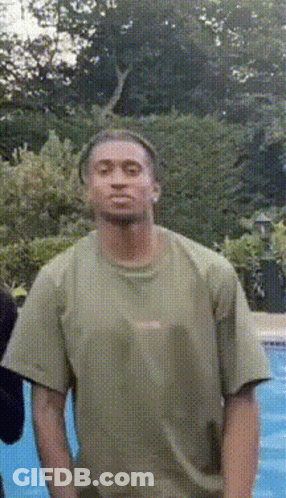 A Man In A Green Shirt Is Standing In Front Of A Swimming Pool GIF