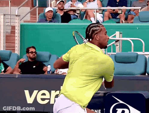A Man In A Green Shirt Is Swinging A Tennis Racket In Front Of A Sign That Says Ver GIF