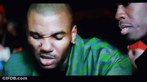 A Man In A Green Shirt Is Talking To Another Man In A Dark Room GIF