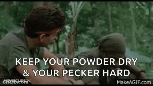 A Man In A Green Shirt Is Talking To Another Man In A Forest While Holding A Stick . GIF
