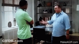 A Man In A Green Shirt Is Talking To Another Man In A Living Room . GIF