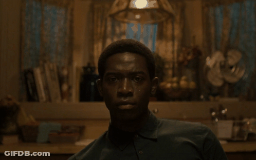 A Man In A Green Shirt Looks At The Camera In A Dark Room GIF