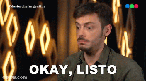 A Man In A Green Shirt Says Okay Listo In Front Of A Neon Sign GIF