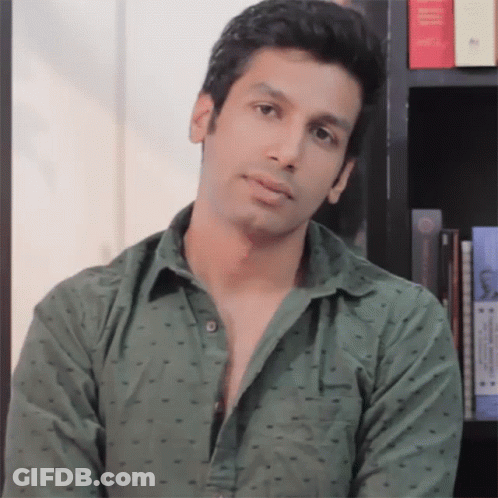 A Man In A Green Shirt Stands In Front Of A Book Shelf GIF