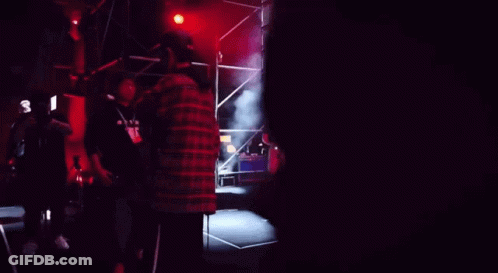 A Man In A Green Shirt Stands In Front Of A Crowd Of People GIF