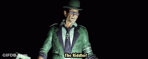 A Man In A Green Suit And Hat Is Holding A Cane With The Words The Riddler Written On It . GIF