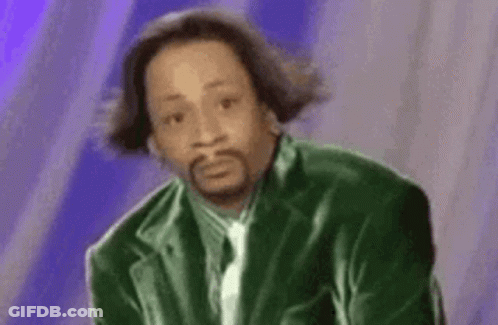 A Man In A Green Suit And Tie Is Sitting Down And Making A Funny Face . GIF