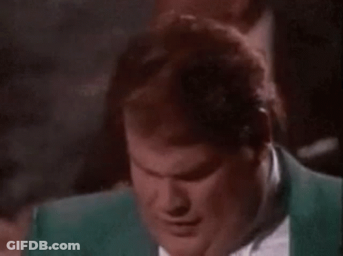 A Man In A Green Suit And Tie Is Smiling While Sitting In A Dark Room . GIF