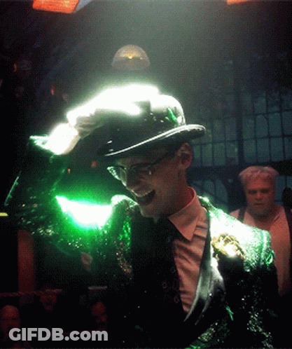 A Man In A Green Suit And Top Hat Is Holding A Green Object In His Hand GIF