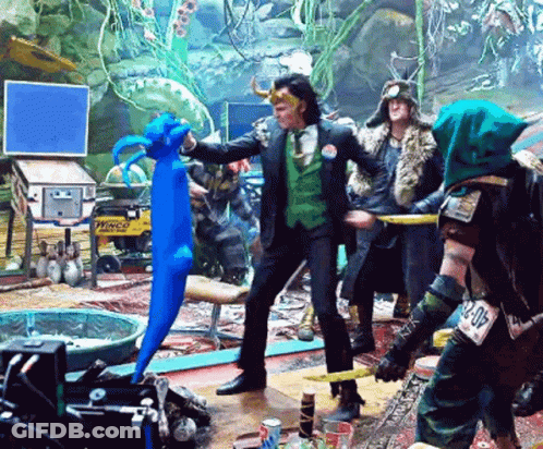 A Man In A Green Suit Is Holding A Blue Stuffed Animal In A Room With Other People GIF