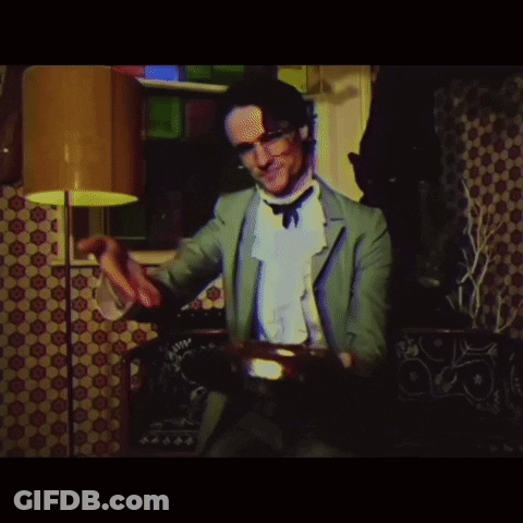A Man In A Green Suit Is Playing A Drum In A Room GIF