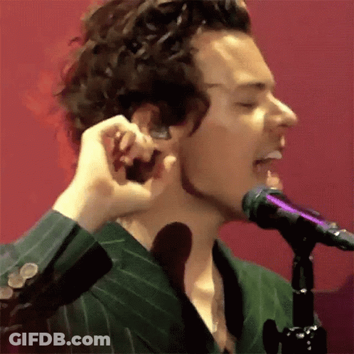A Man In A Green Suit Is Singing Into A Microphone While Holding His Ear . GIF