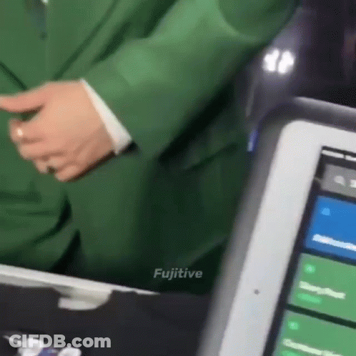 A Man In A Green Suit Is Standing Next To A Tablet With The Word Fugitive On The Bottom GIF