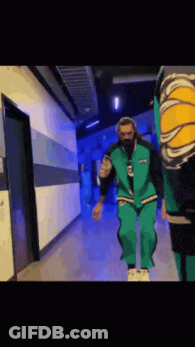 A Man In A Green Suit Is Walking Down A Hallway . GIF