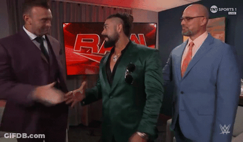 A Man In A Green Suit Talks To Two Other Men In Suits GIF