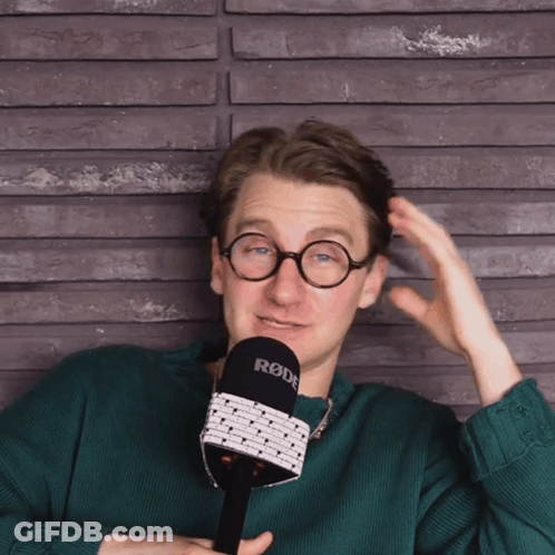 A Man In A Green Sweater Holds A Rode Microphone GIF