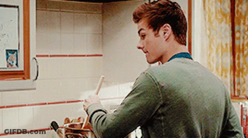 A Man In A Green Sweater Is Stirring Something In A Pot GIF