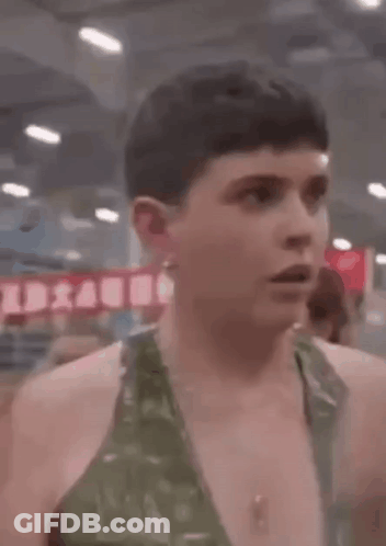 A Man In A Green Tank Top Is Standing In A Gym And Looking At The Camera . GIF