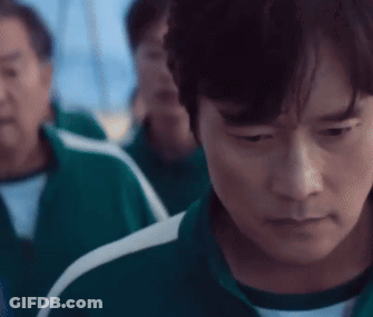 A Man In A Green Tracksuit Is Looking Down At Something While Standing In Front Of A Group Of People . GIF