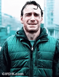 A Man In A Green Vest Is Crying While Standing In Front Of A Building . GIF