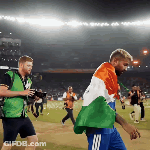 A Man In A Green Vest Is Taking A Picture Of Another Man In A Blue Shirt GIF