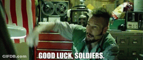 A Man In A Green Vest Says Good Luck Soldiers In Front Of A Red And White Striped Wall GIF