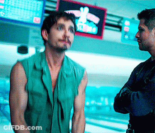 A Man In A Green Vest Stands Next To Another Man In Front Of A Bowling Alley GIF