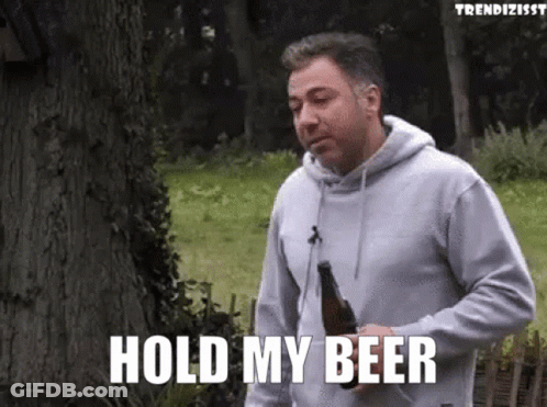 A Man In A Grey Hoodie Is Holding A Bottle Of Beer And Saying Hold My Beer GIF