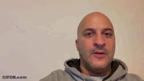A Man In A Grey Hoodie Is Standing In Front Of A Sign That Says Thank You GIF