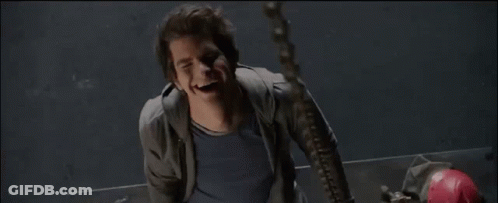 A Man In A Grey Jacket And Blue Shirt Smiles While Hanging From A Chain GIF