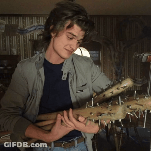 A Man In A Grey Jacket Is Holding A Bunch Of Sticks With Nails Sticking Out Of Them GIF