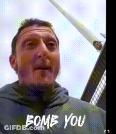 A Man In A Grey Jacket Says " Bomb You " In White Letters GIF