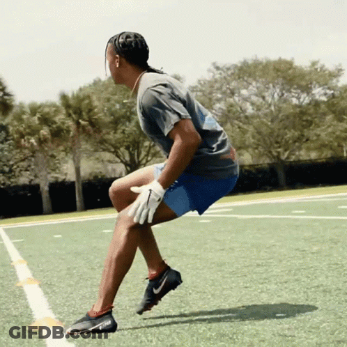 A Man In A Grey Shirt And Blue Shorts Is Squatting On A Field GIF