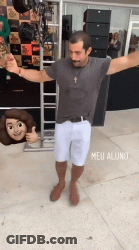 A Man In A Grey Shirt And White Shorts Is Dancing In Front Of A Sign That Says Meu Aluno On It GIF