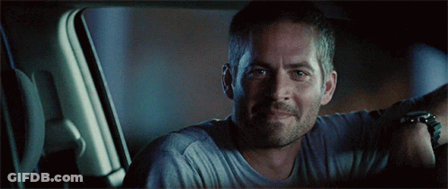 A Man In A Grey Shirt Is Smiling In A Car GIF