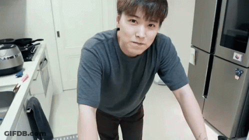 A Man In A Grey Shirt Is Standing In A Kitchen With A Lg Refrigerator In The Background GIF