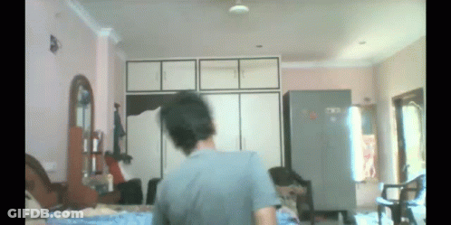 A Man In A Grey Shirt Is Standing In A Room GIF