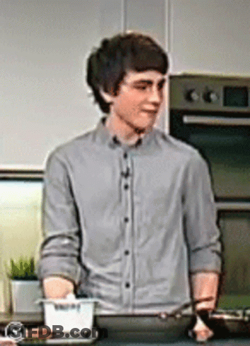 A Man In A Grey Shirt Is Standing In Front Of A Pan GIF