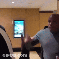 A Man In A Grey Shirt Is Standing In Front Of A Wall With A Picture On It GIF