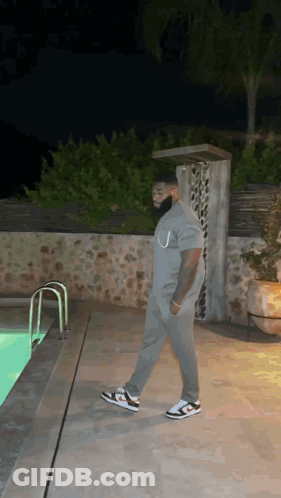 A Man In A Grey Shirt Is Walking By A Swimming Pool At Night . GIF