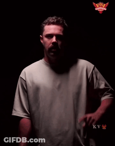 A Man In A Grey Shirt Stands In Front Of A Sign That Says Play With Fire GIF