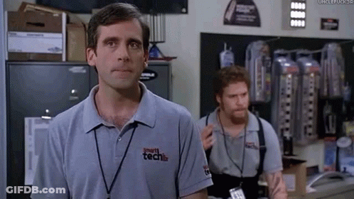 A Man In A Grey Shirt With A Lanyard Around His Neck Is Standing In A Room With Two Other Men . GIF
