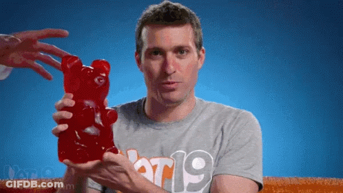A Man In A Grey Shirt With The Number 19 On It Holds A Large Gummy Bear GIF
