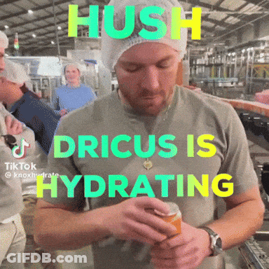 A Man In A Grey Shirt With The Words Hush Dricus Is Hydrating On The Front GIF